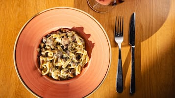 Ein Teller Pasta mit cremiger Soße, dazu liegen Messer und Gabel auf einer Holztischplatte.