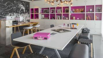 Ein moderner Arbeitsraum mit einem weißen Tisch, schwarzen und hölzernen Stühlen, einem pinken Koffer und einer schwarzen Bank.