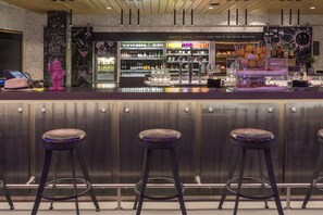Zona de bar con taburetes, estantes llenos de bebidas y un cartel en la pizarra.