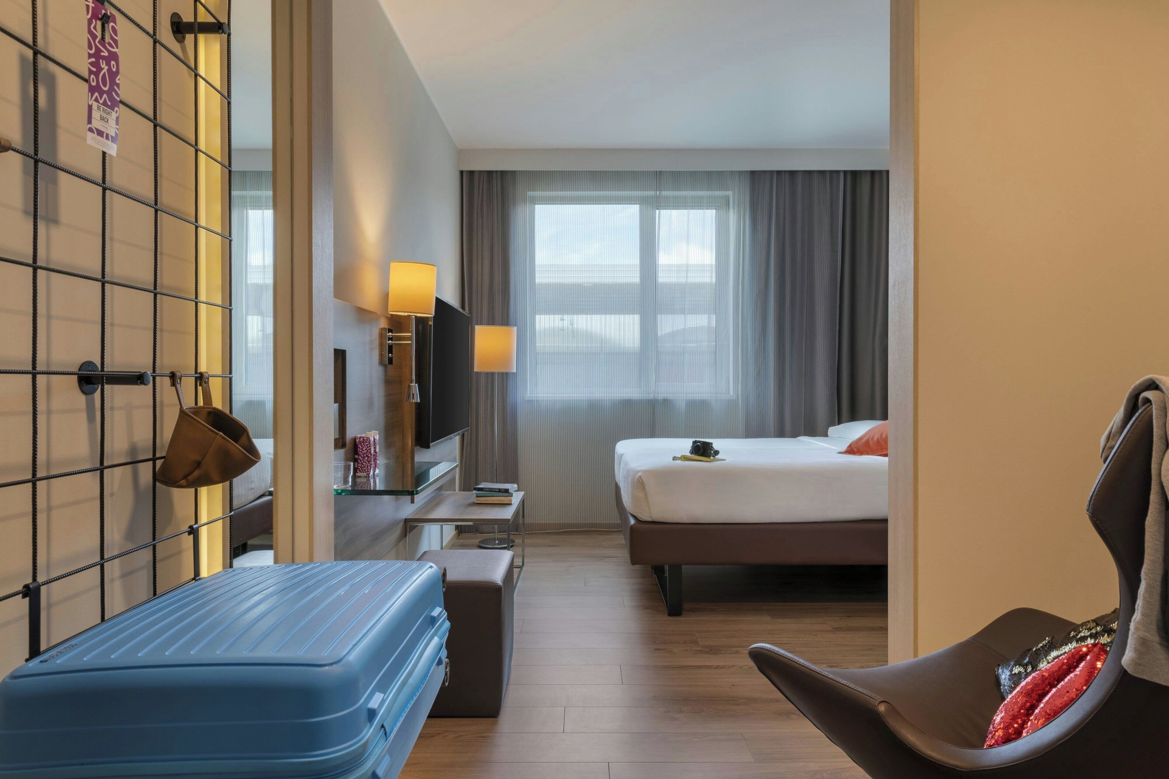 Een hotelkamer met een bed, een bureau met een lamp, een televisie en een stoel.