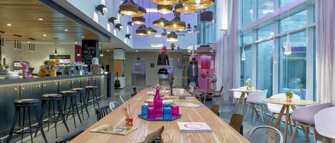 A modern restaurant with a long wooden table, bar stools, and pendant lighting.
