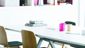 A modern meeting room with a white table, wooden chairs, and a bookshelf with various items.
