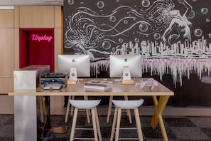 A modern workspace with two Apple iMacs, a printer, and a book titled 'LOVE SHOE'. - MOXY Milan Malpensa Airport (Somma Lombardo)