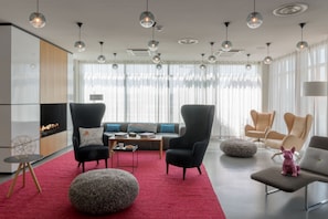 Una sala de estar moderna con alfombra roja, sillas negras y beige, un otoman redondo y una pequeña estatua de un perro rosa.