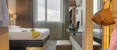 A hotel room with a bed, bedside table, lamp, and a window with curtains.