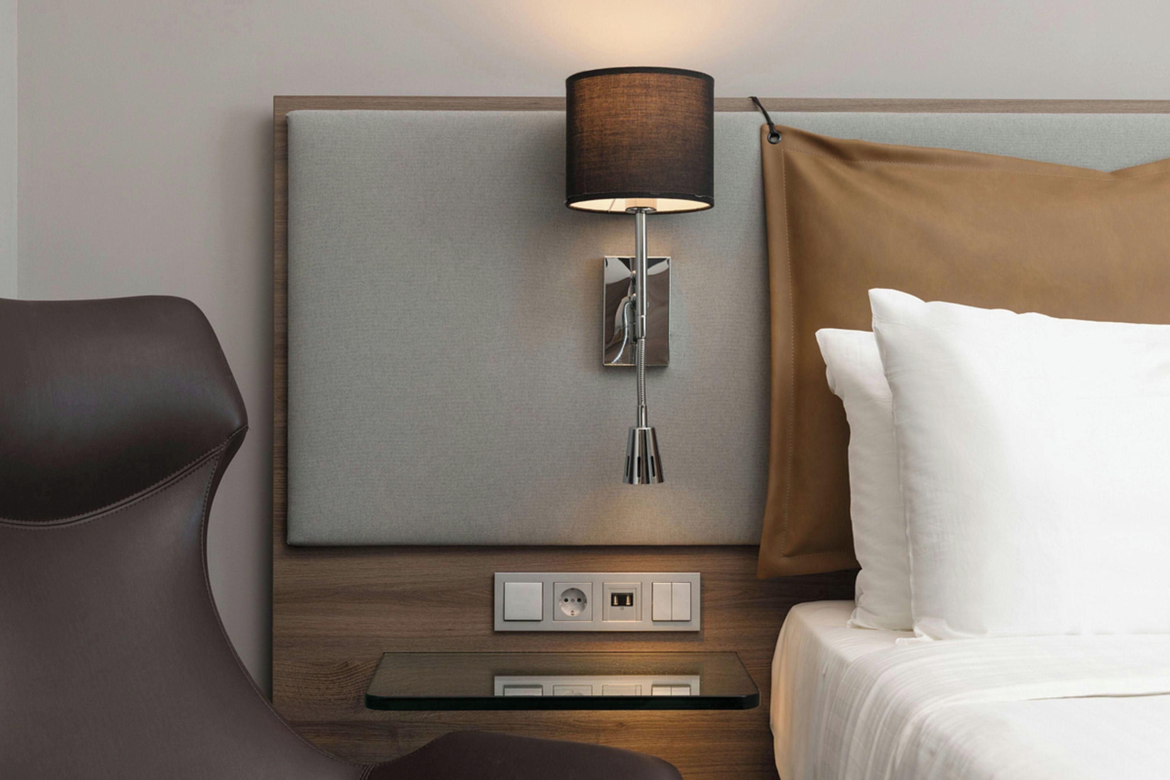 Una habitación de hotel con una cama, una mesita de noche, una lámpara y un enchufe.