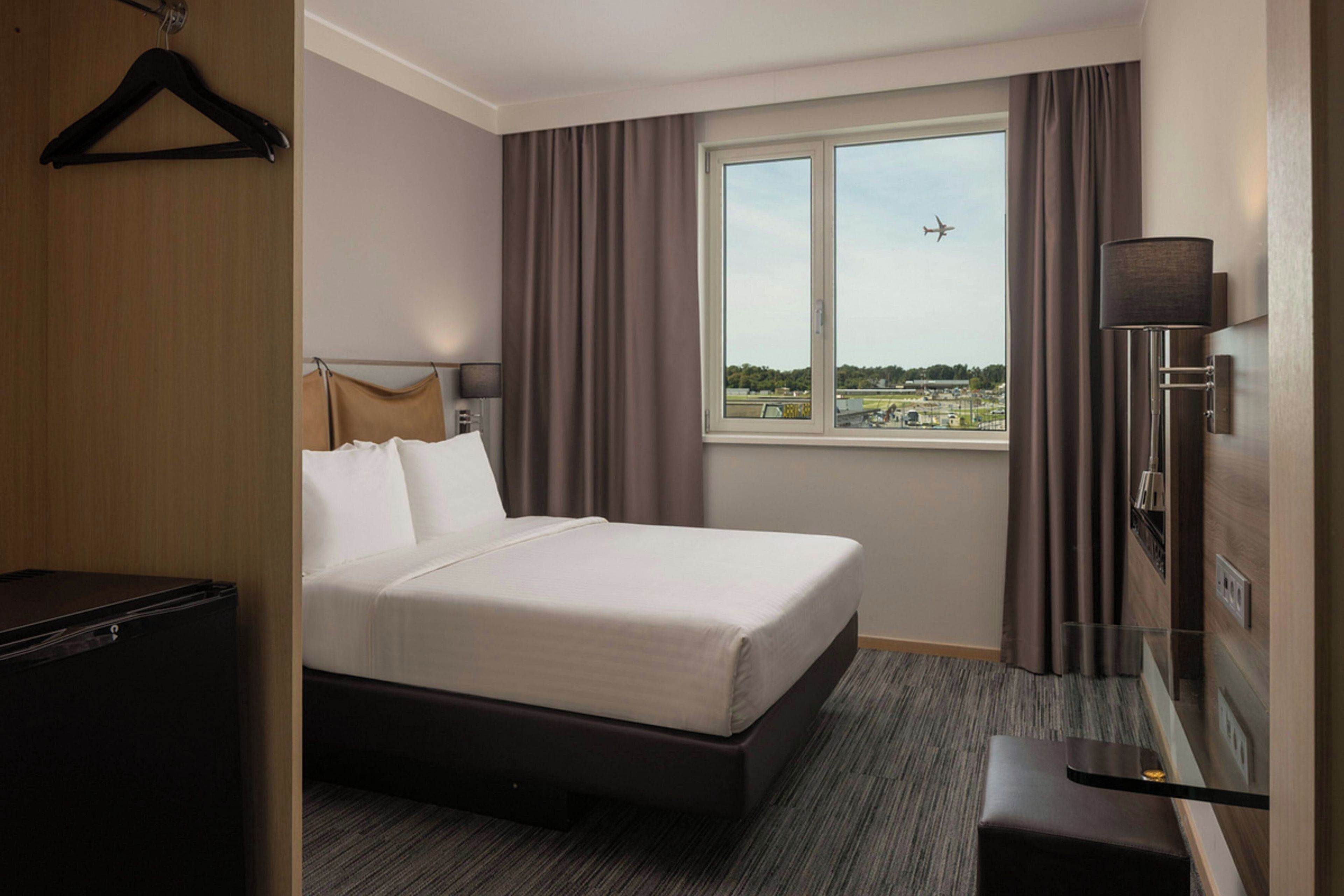 Une chambre d’hôtel avec un lit, un bureau, une télévision et une fenêtre donnant sur un aéroport.