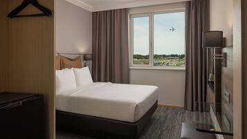 Une chambre d’hôtel avec un lit, un bureau, une télévision et une fenêtre donnant sur un aéroport.