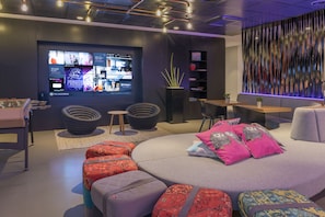 A modern lounge area with a large digital display, comfortable seating, and a decorative wall. - MOXY Milan Malpensa Airport (Somma Lombardo)
