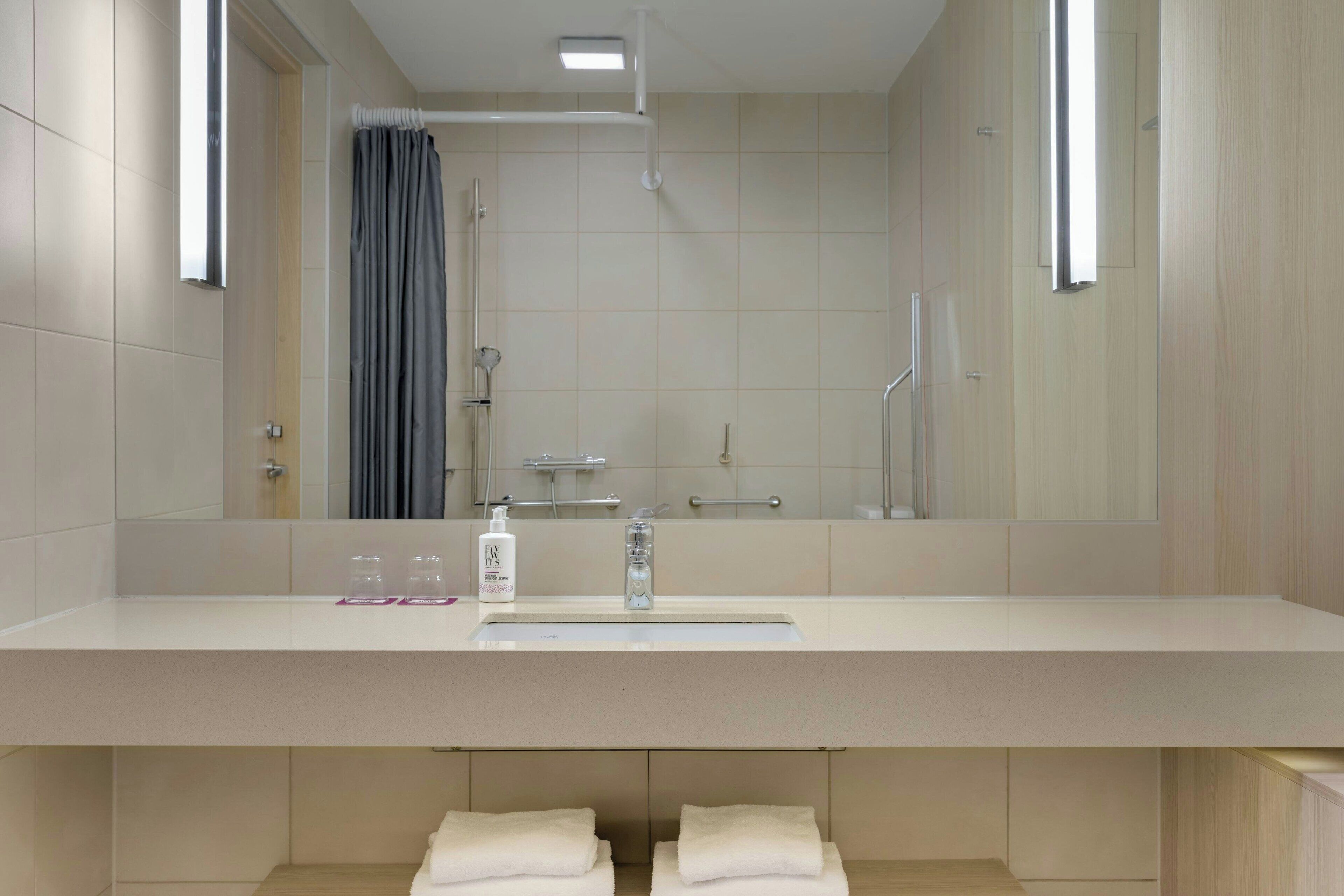 A modern bathroom with a large mirror, a sink, and a shower.