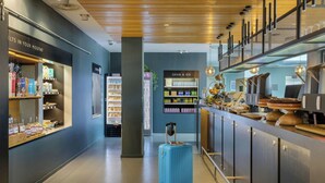 A modern hotel lobby with a blue suitcase, a 'Grab & Go' snack bar, and a 'ELTS IN YOUR MOUTH!' beverage station.