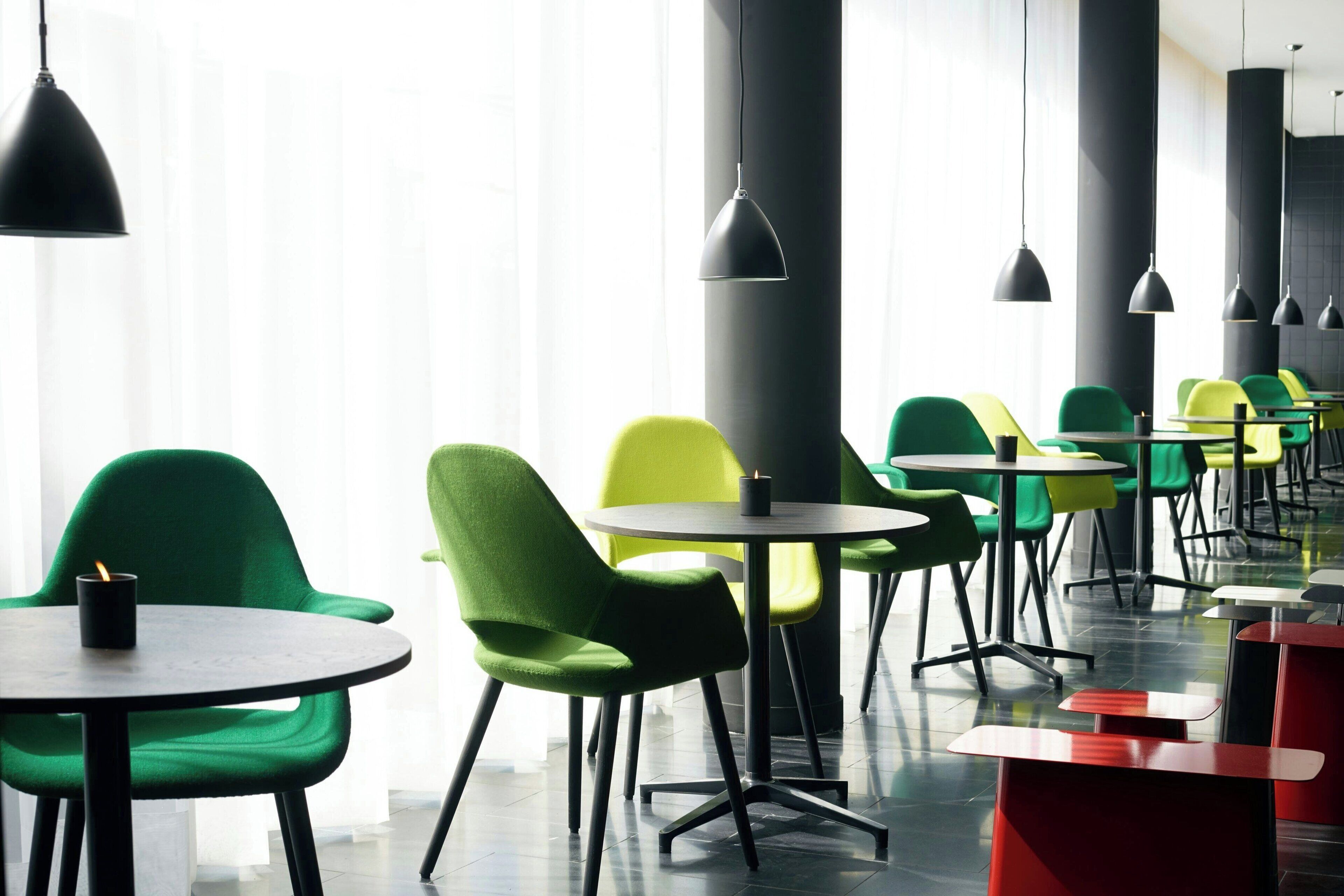 Un comedor moderno con mesas y sillas redondas, ventanas amplias e iluminación colgante.