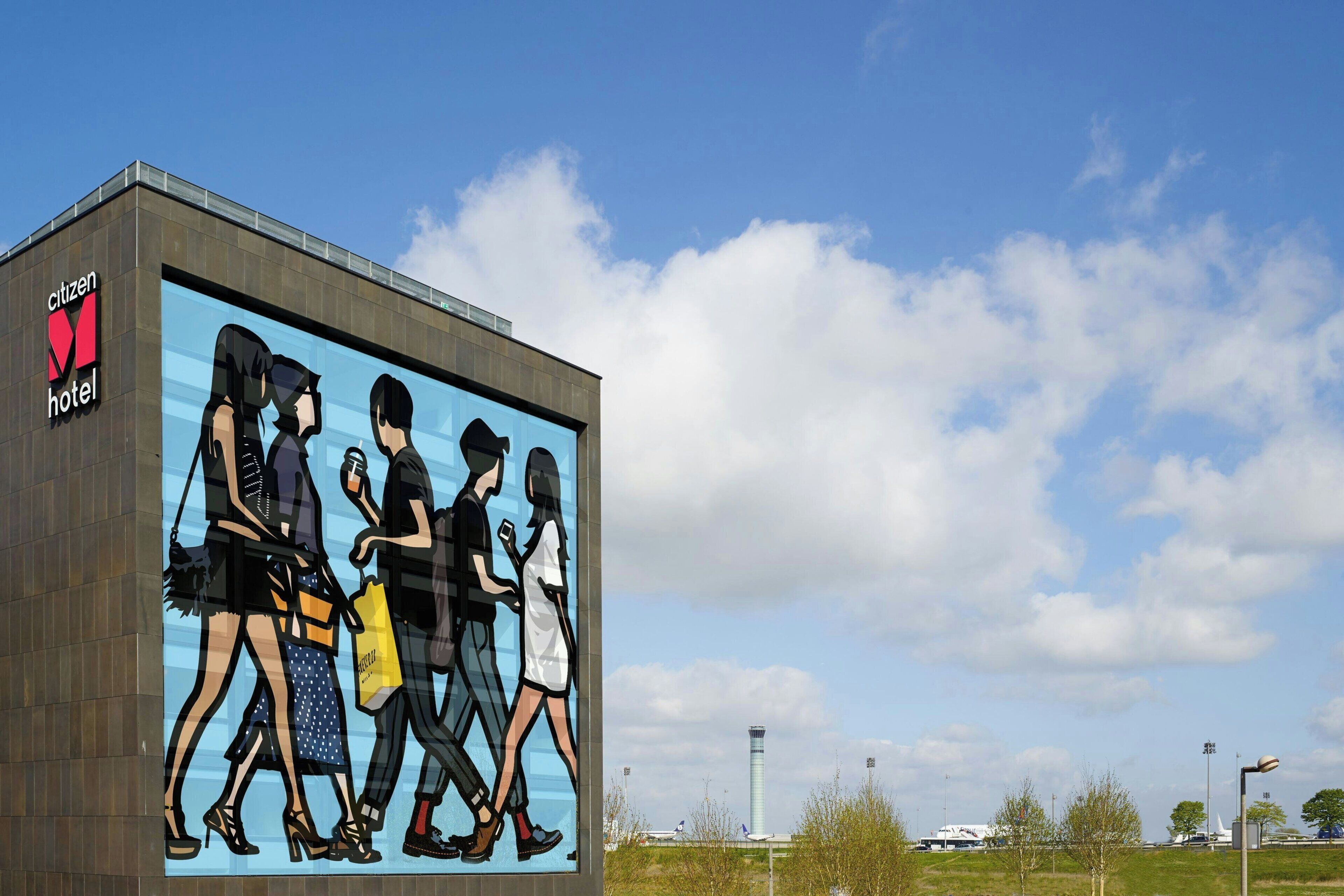 A building with a large mural of people walking, a "Citizen Hotel" sign, and a clear sky with clouds.
