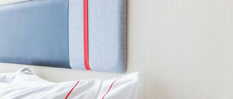 A hotel room with a bed, white bedding, a bedside table, and a wall-mounted device.