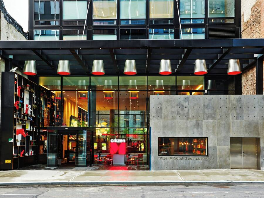 A modern hotel entrance with a glass facade, red accents, and a prominent 'Citizen Hotel Times Square' sign.