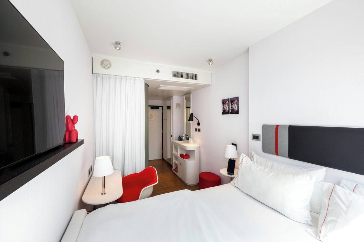 Quarto de hotel moderno com uma cama grande, uma escrivaninha, uma cadeira e uma televisão.