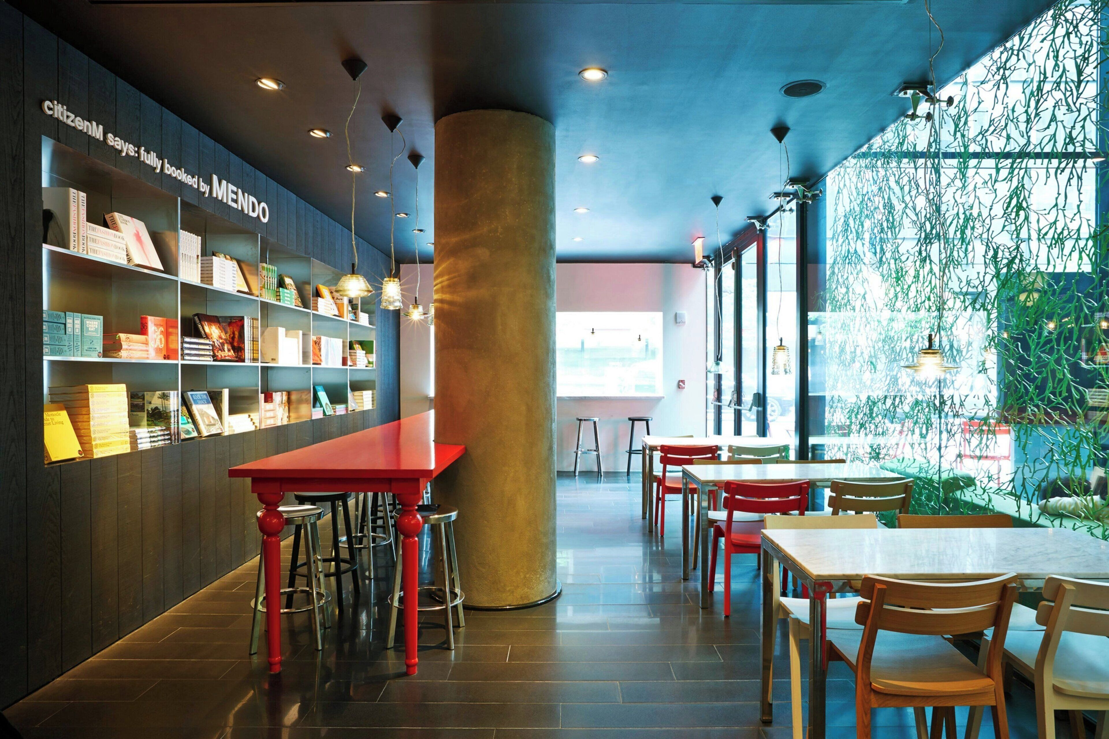 A modern interior with a red table and chairs, a bookshelf with books, and a large pillar.