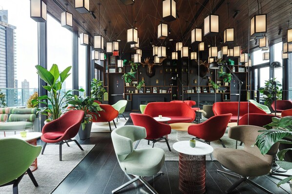 Un salón moderno con sillas rojas y verdes, una chimenea y vistas a la ciudad.