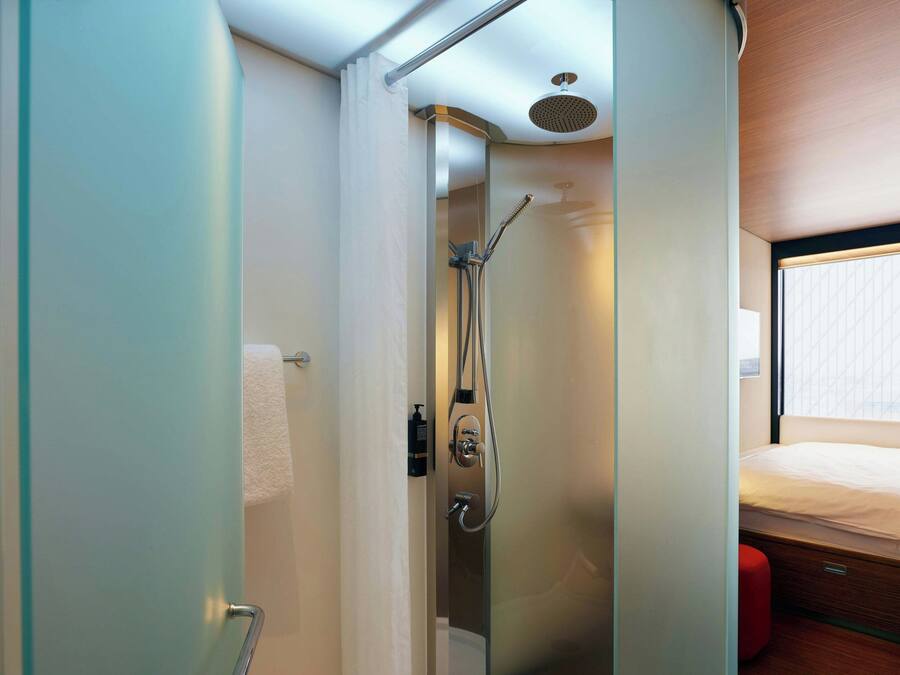 A modern bathroom with a glass shower enclosure, a toilet, and a bed with a window view.