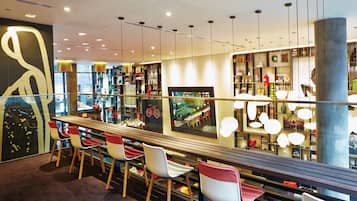 Uma área de bar moderna com um balcão comprido, várias cadeiras e guarda-corpo de vidro.