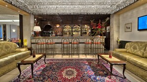 Een bar met een kroonluchter, barstoelen en een kamerbreed tapijt met een patroon.