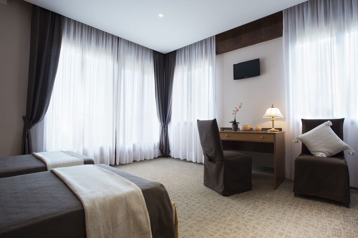 Ein Hotelzimmer mit zwei Betten, einem Schreibtisch, einem Stuhl, einer Lampe und einem Fernseher an der Wand.