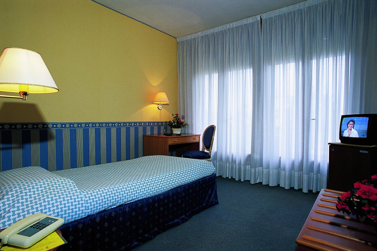 Ein Hotelzimmer mit einem Bett, einem Schreibtisch mit Lampe, einem Fernseher und einem Telefon.