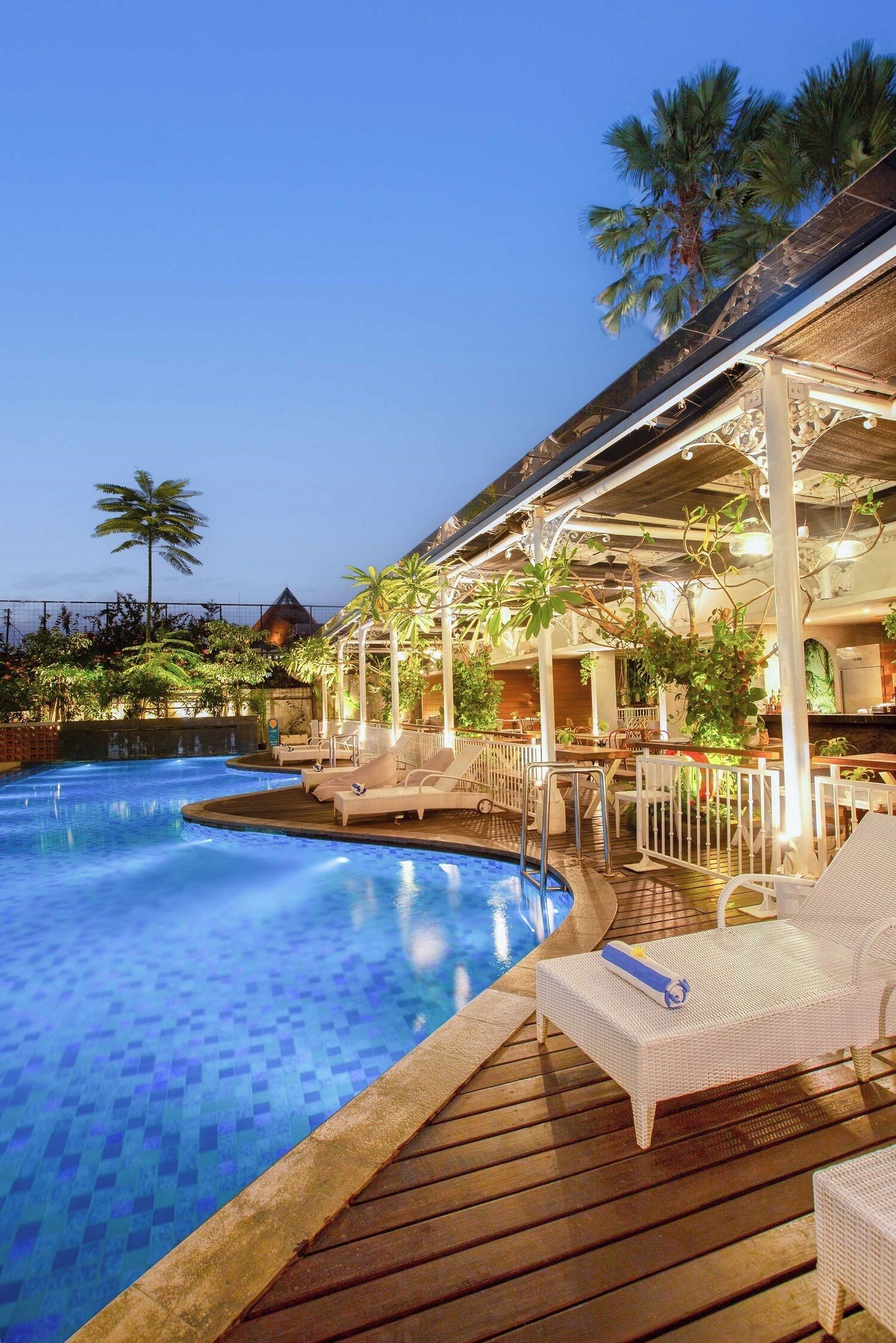 A poolside area with lounge chairs, a wooden deck, and a covered seating area with plants.