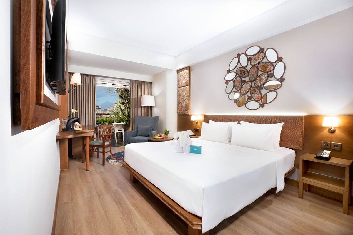 A hotel room with a bed, a desk, a chair, a TV, and a decorative wall piece.