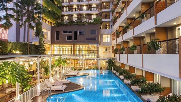Un hotel con piscina, varios balcones y una fachada bien iluminada.