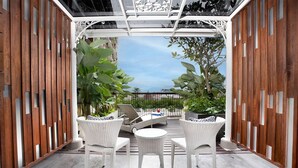 Un espacio de estar al aire libre techado con mobiliario de mimbre y vista a la ciudad.