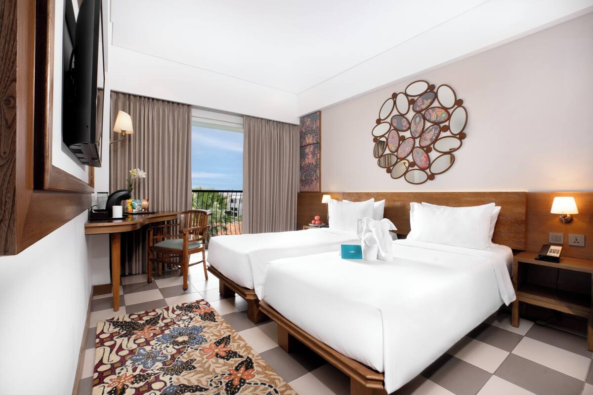A hotel room with two beds, a desk, a chair, a TV, and a decorative wall piece.