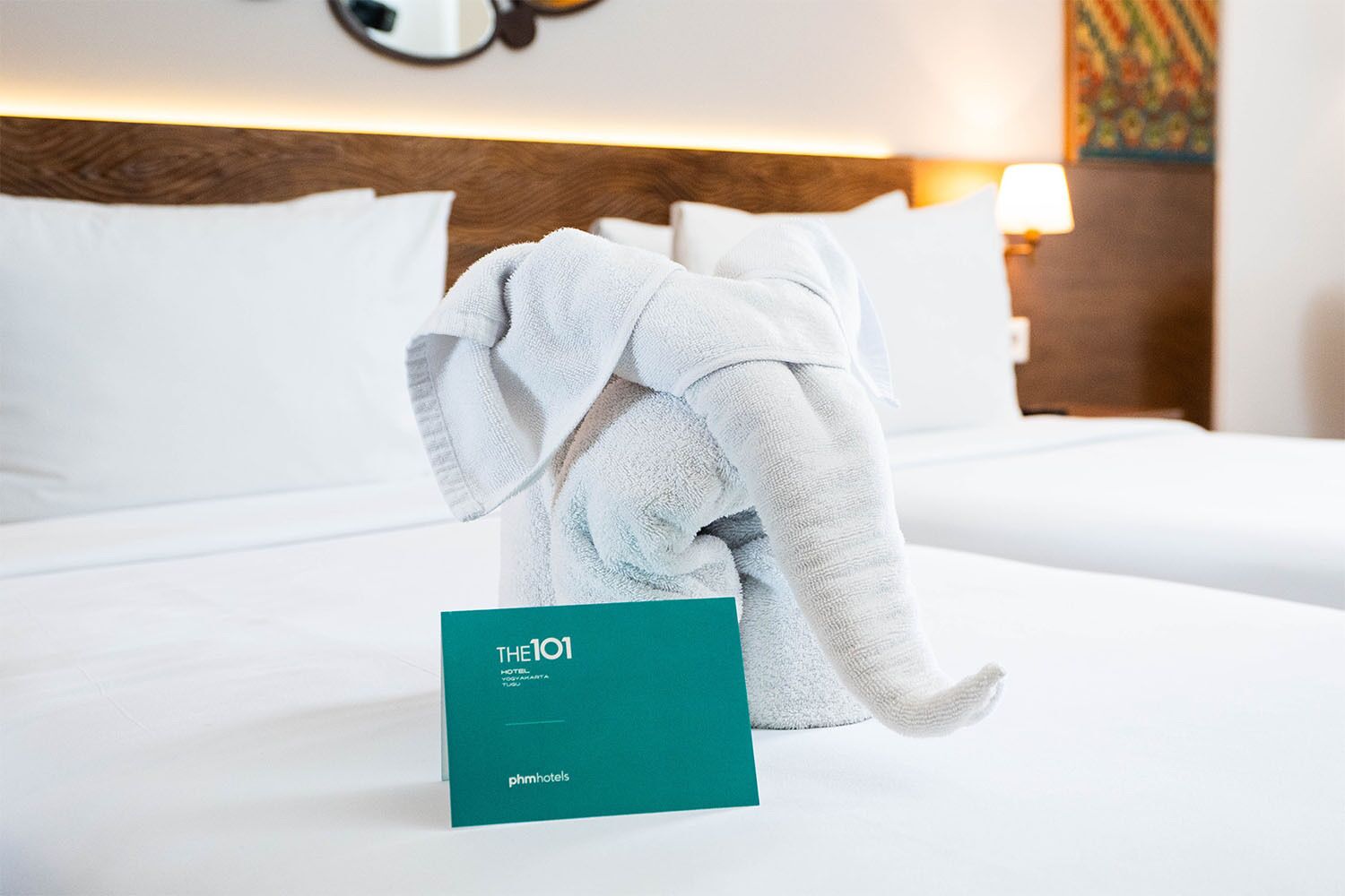 Een hotelkamer met een opgemaakt bed, een handdoek en een bordje met de naam van het hotel.