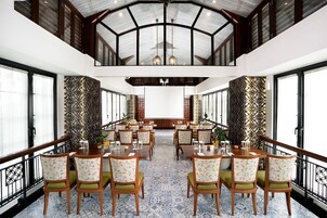 A spacious dining area with high ceilings and large windows, featuring wooden tables and chairs with green cushions.