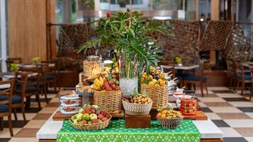 Mesa de buffet con diversas frutas y cestas, una planta en maceta y suelo a cuadros.