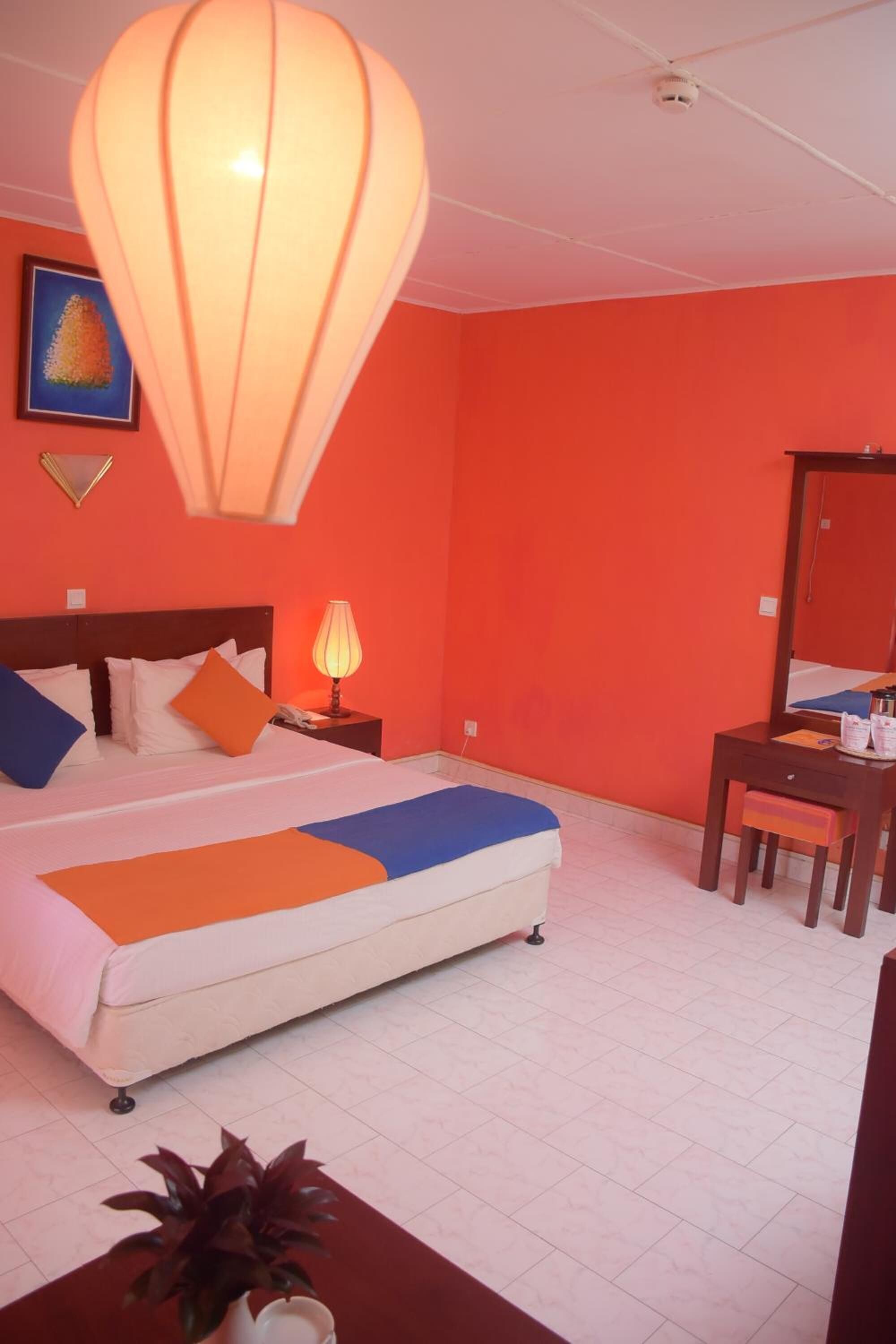 A room with a bed, a desk, a chair, a lamp, and a large hanging light fixture.