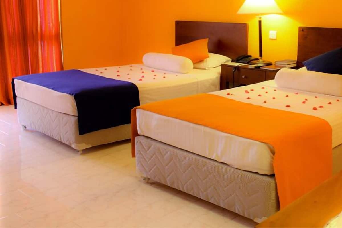 Ein Hotelzimmer mit zwei Betten, jeweils mit Kissen und Decke. Ein Nachttisch mit Lampe und Telefon ist vorhanden.