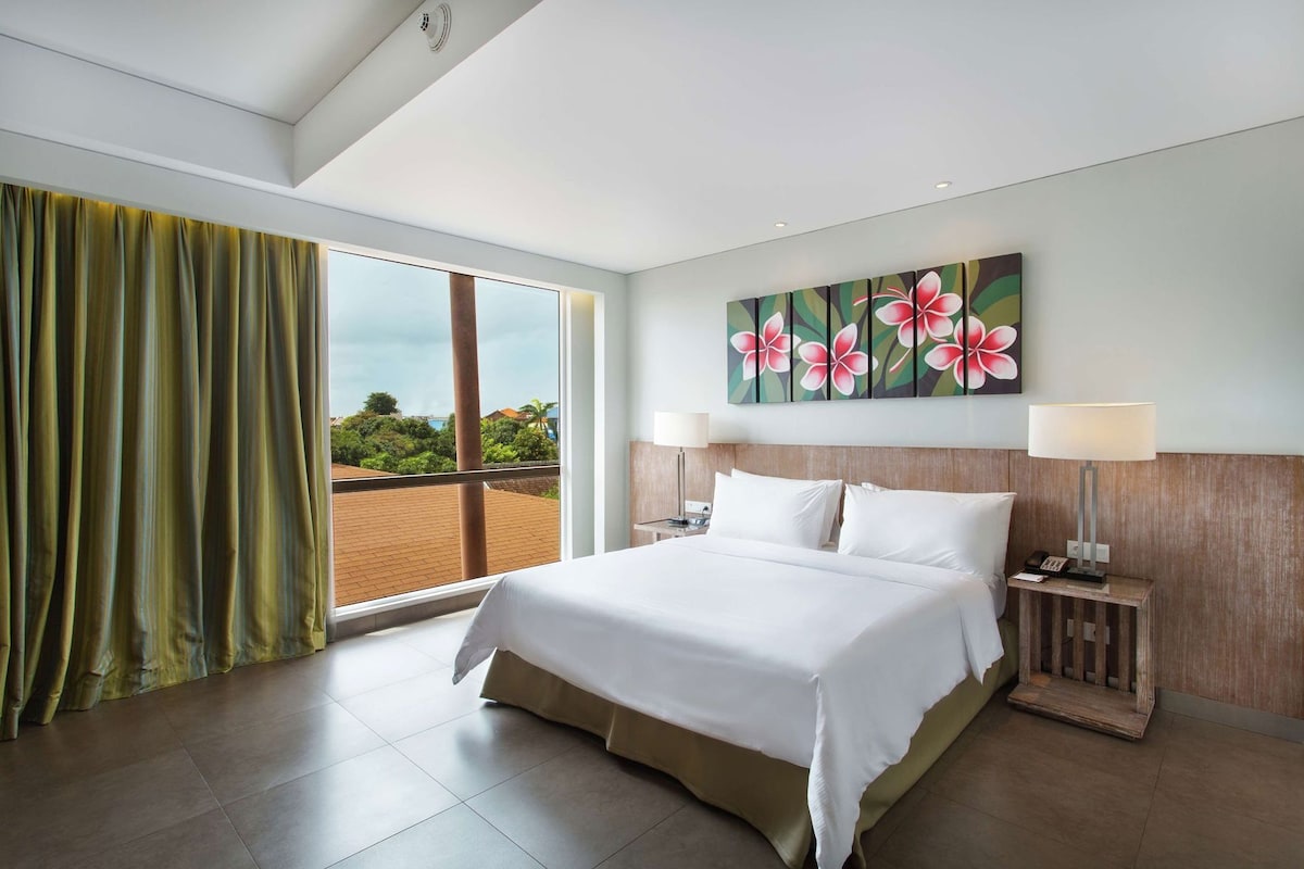 Habitación de hotel con una cama grande, vistas al exterior y un cuadro de flores en la pared.