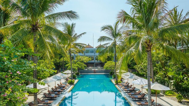 A pool with lounge chairs and umbrellas, surrounded by palm trees and greenery. - Hilton Garden Inn Bali Ngurah Rai Airport (Tuban)