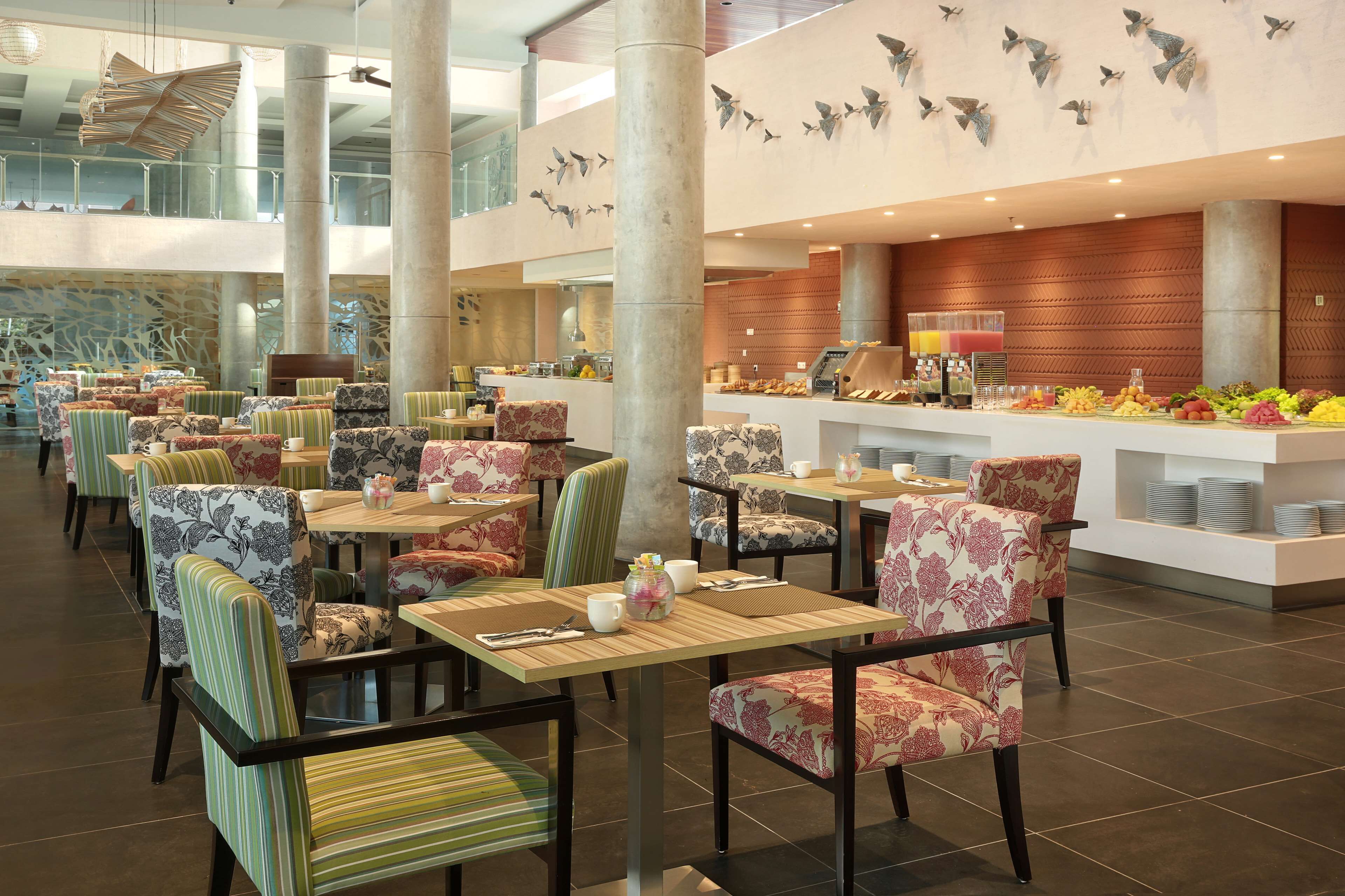 A spacious hotel lobby with multiple dining areas, a central buffet, and decorative wall art.