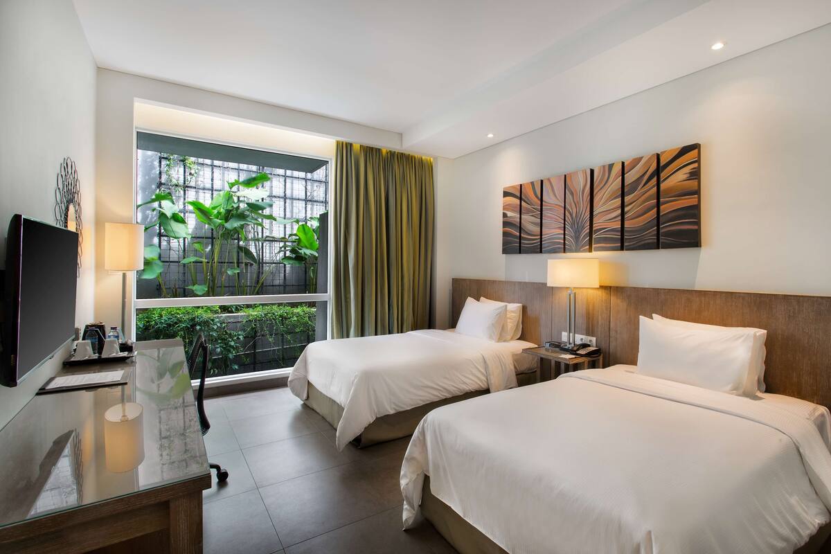 Une chambre d’hôtel avec deux lits, une télévision, un bureau et une fenêtre donnant sur un paysage verdoyant.