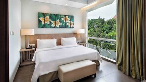 A modern hotel room with a large bed, a bench, a nightstand, a lamp, and a view of greenery through the window. - Hilton Garden Inn Bali Ngurah Rai Airport (Tuban)