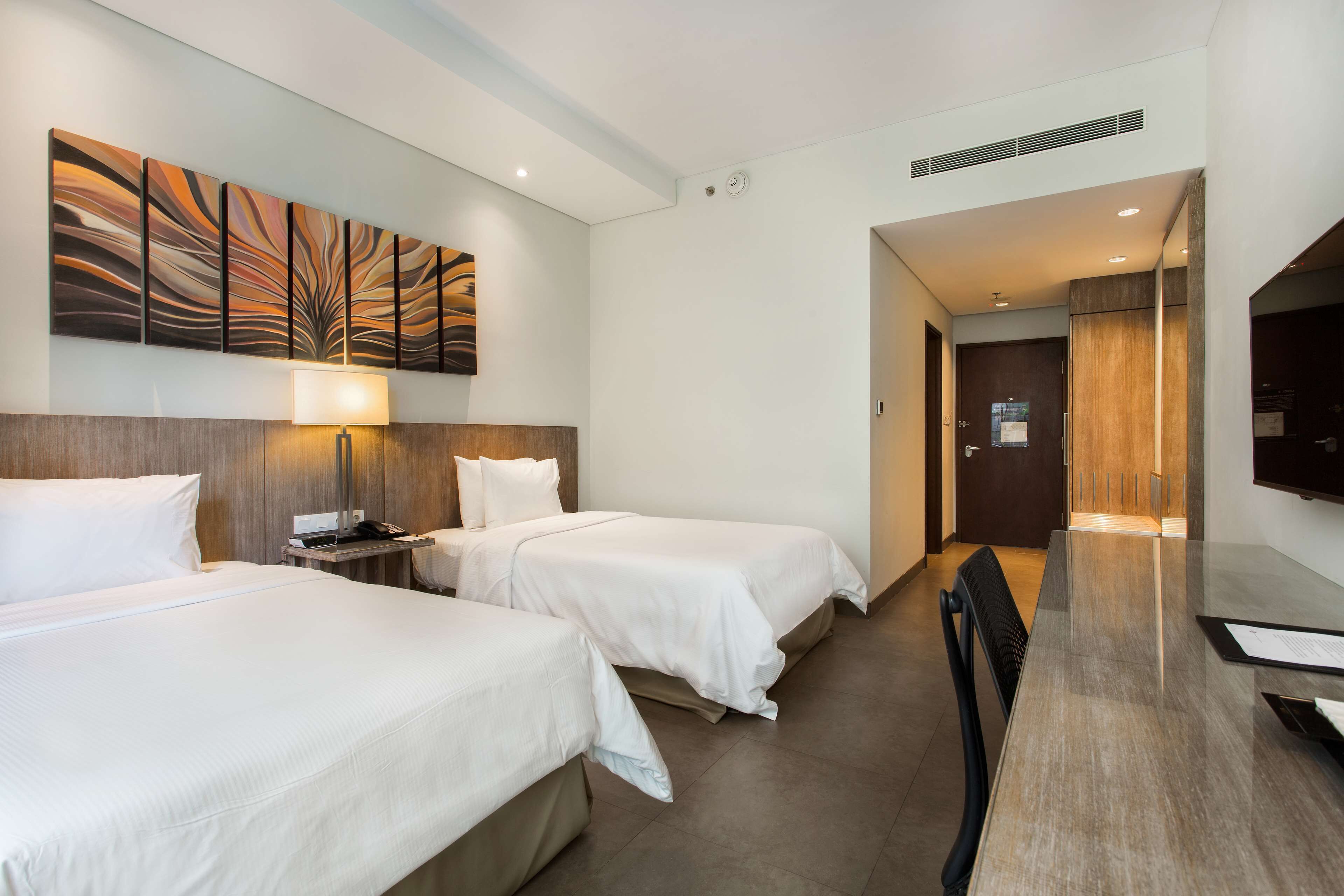 A hotel room with two beds, a desk, a TV, and a painting on the wall.