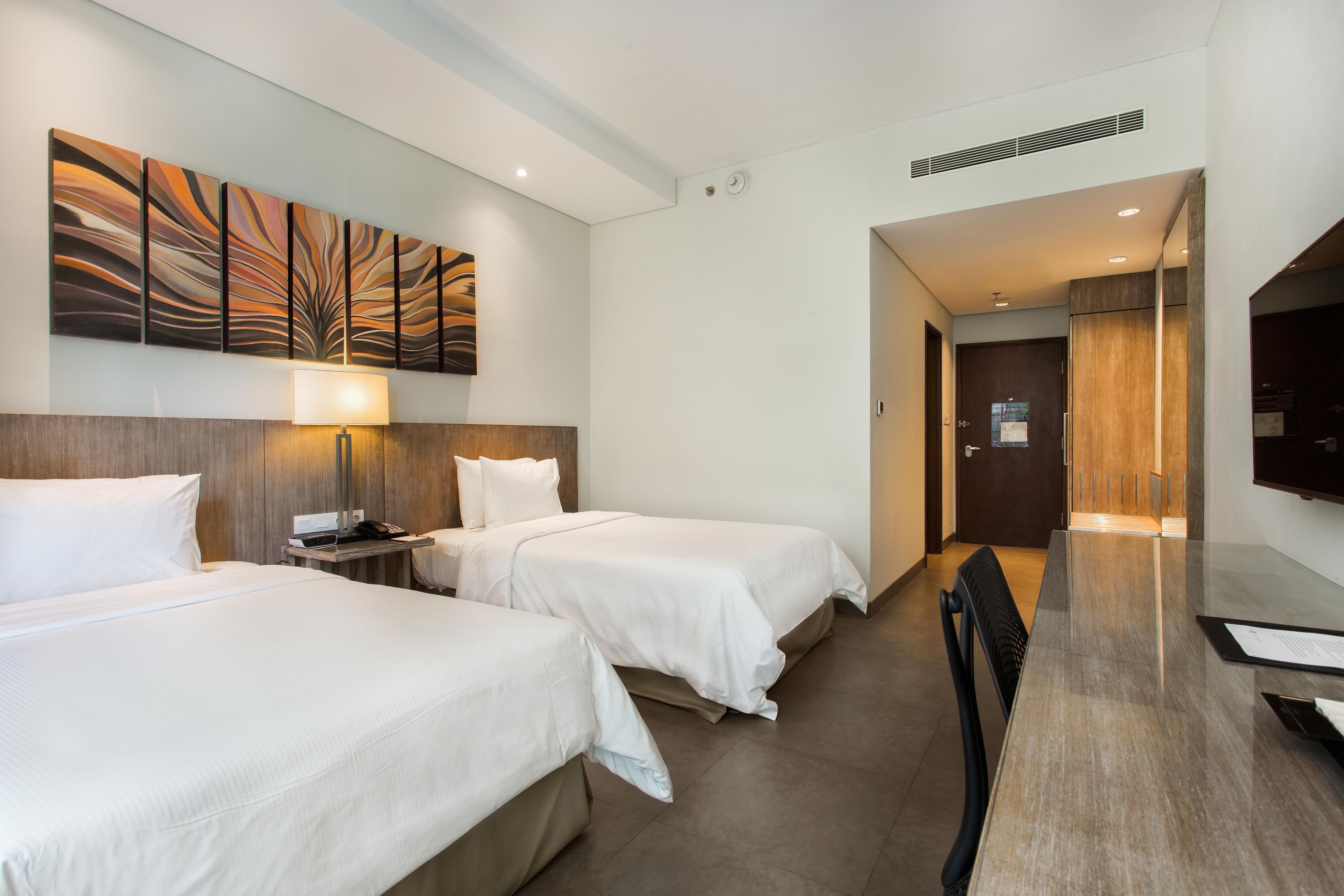 Une chambre d’hôtel avec deux lits, un bureau, une chaise, une télévision et un tableau au mur.
