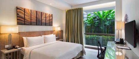A hotel room with a large bed, bedside lamps, a desk with a chair, a TV, and a window with curtains.