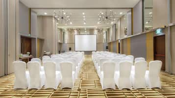 A conference room with rows of white chairs, a large screen, and modern chandeliers.