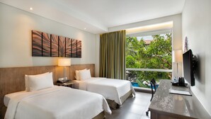 A hotel room with two beds, a desk, a TV, and a window with a view of greenery. - Hilton Garden Inn Bali Ngurah Rai Airport (Tuban)