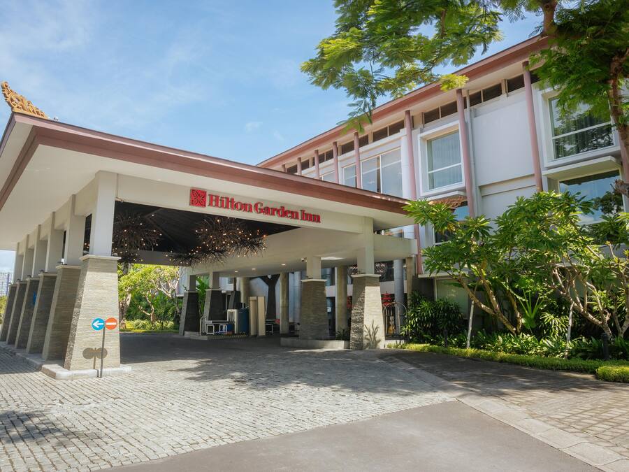 Entrada de hotel con un área cubierta, cartel de Hilton Garden Inn y un camino pavimentado.