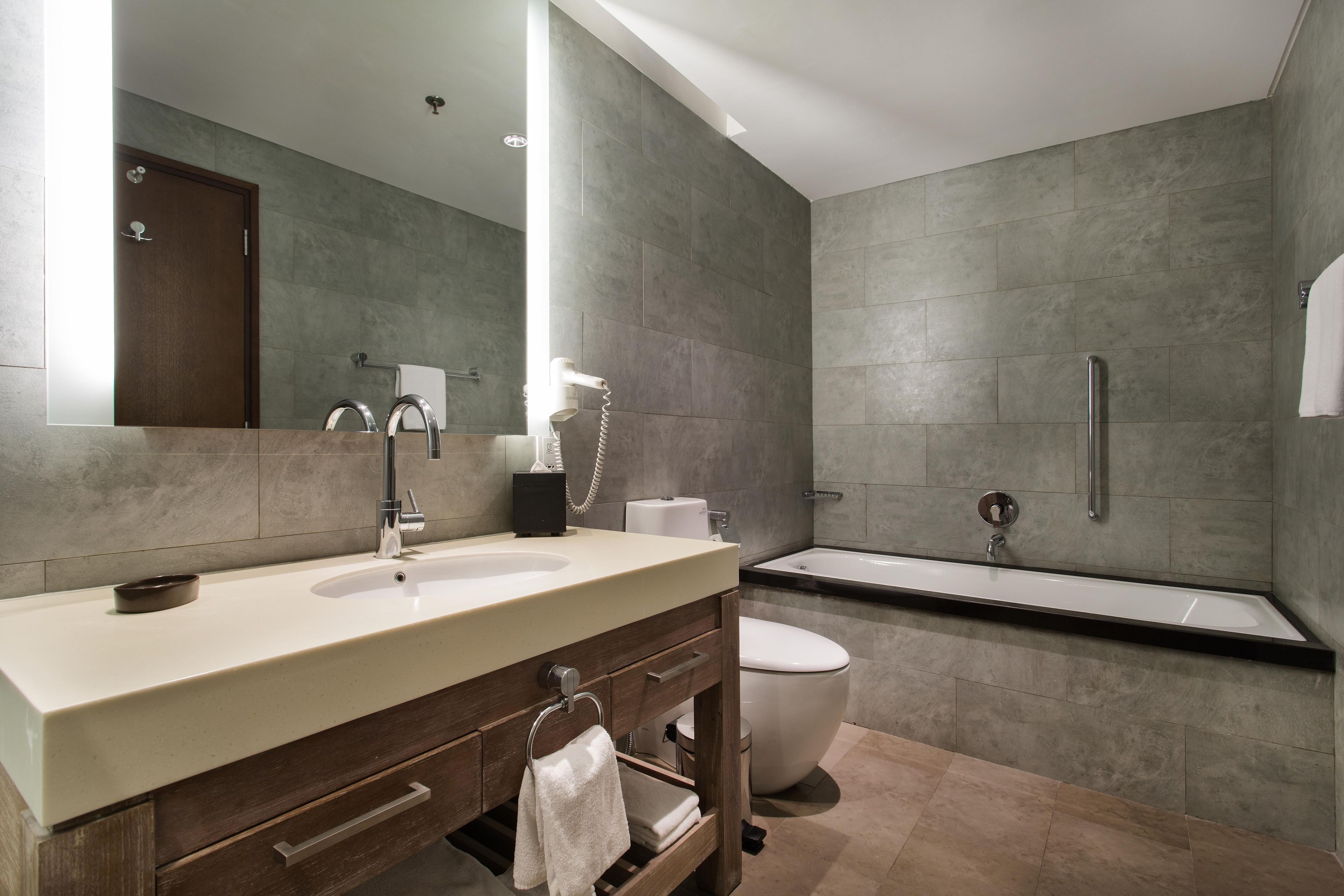 A modern bathroom with a large mirror, a sink, a toilet, and a bathtub.