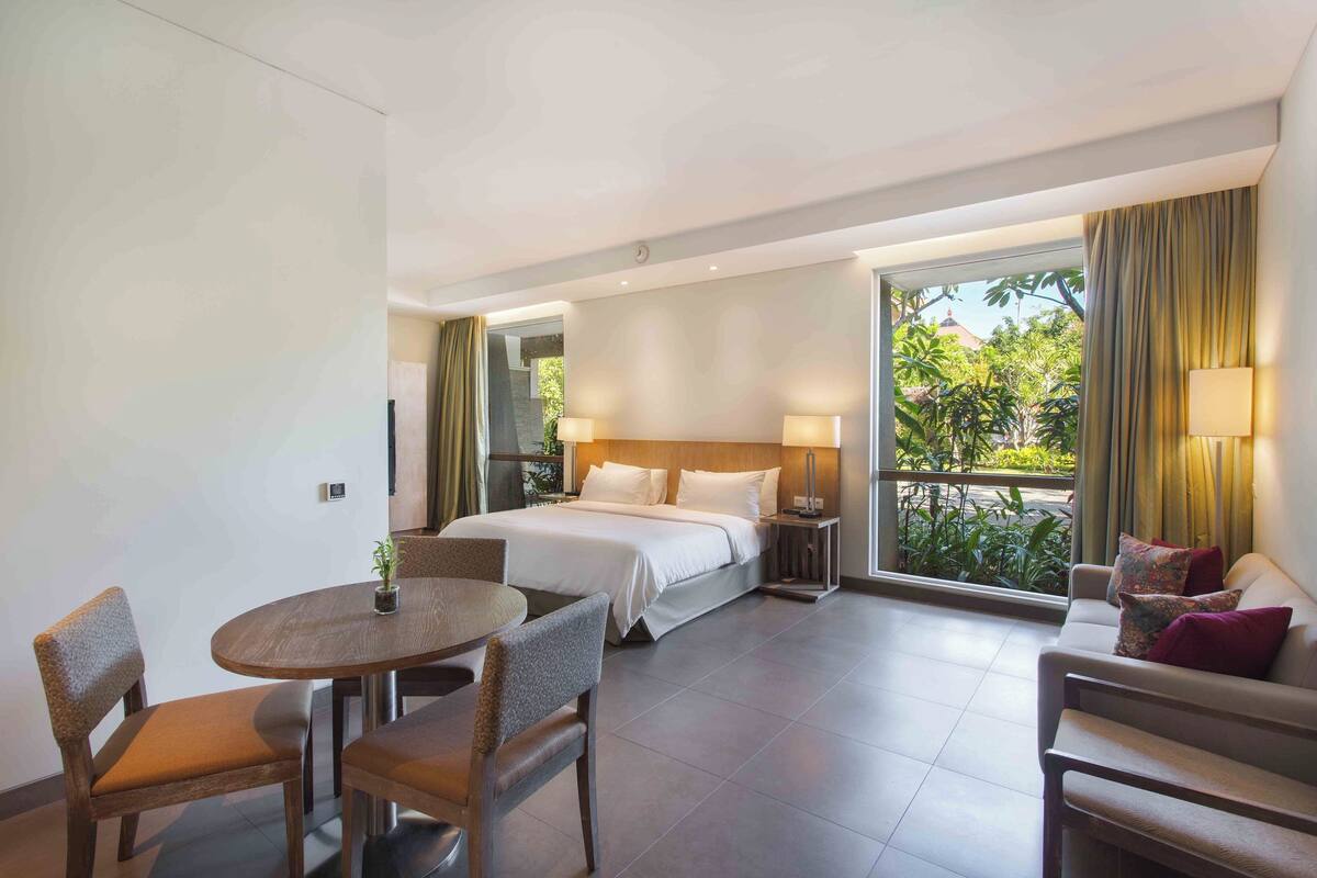Une chambre d’hôtel comprenant un lit, une table à manger avec des chaises, un canapé et un balcon avec des rideaux.